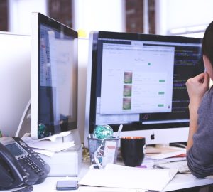 Woman with her back to tyhe camera facing two computer screens thinking
